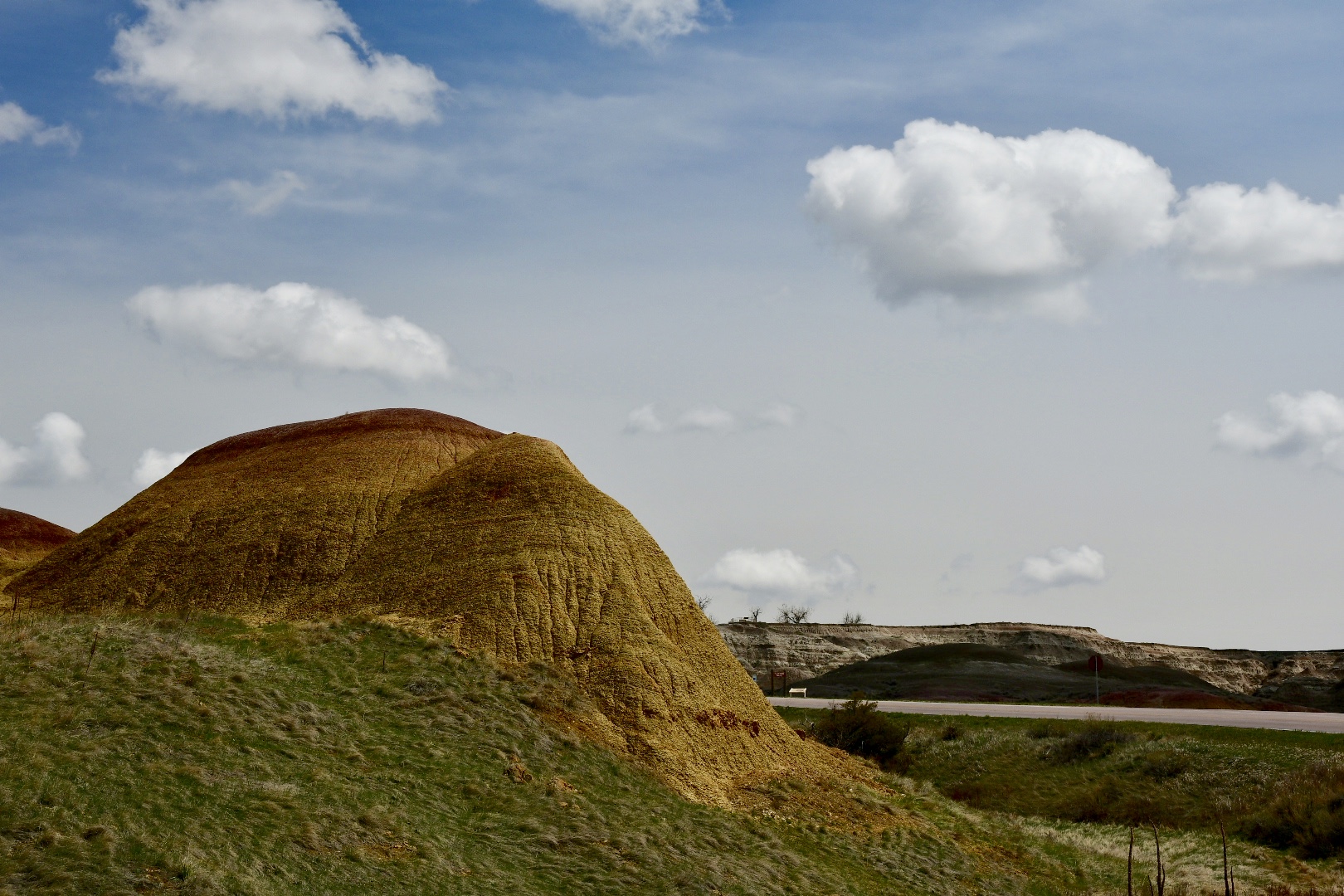 Grünes Gras, gelber Hügel und blauer Himmel mit weißen Wolken im Badlands National Park