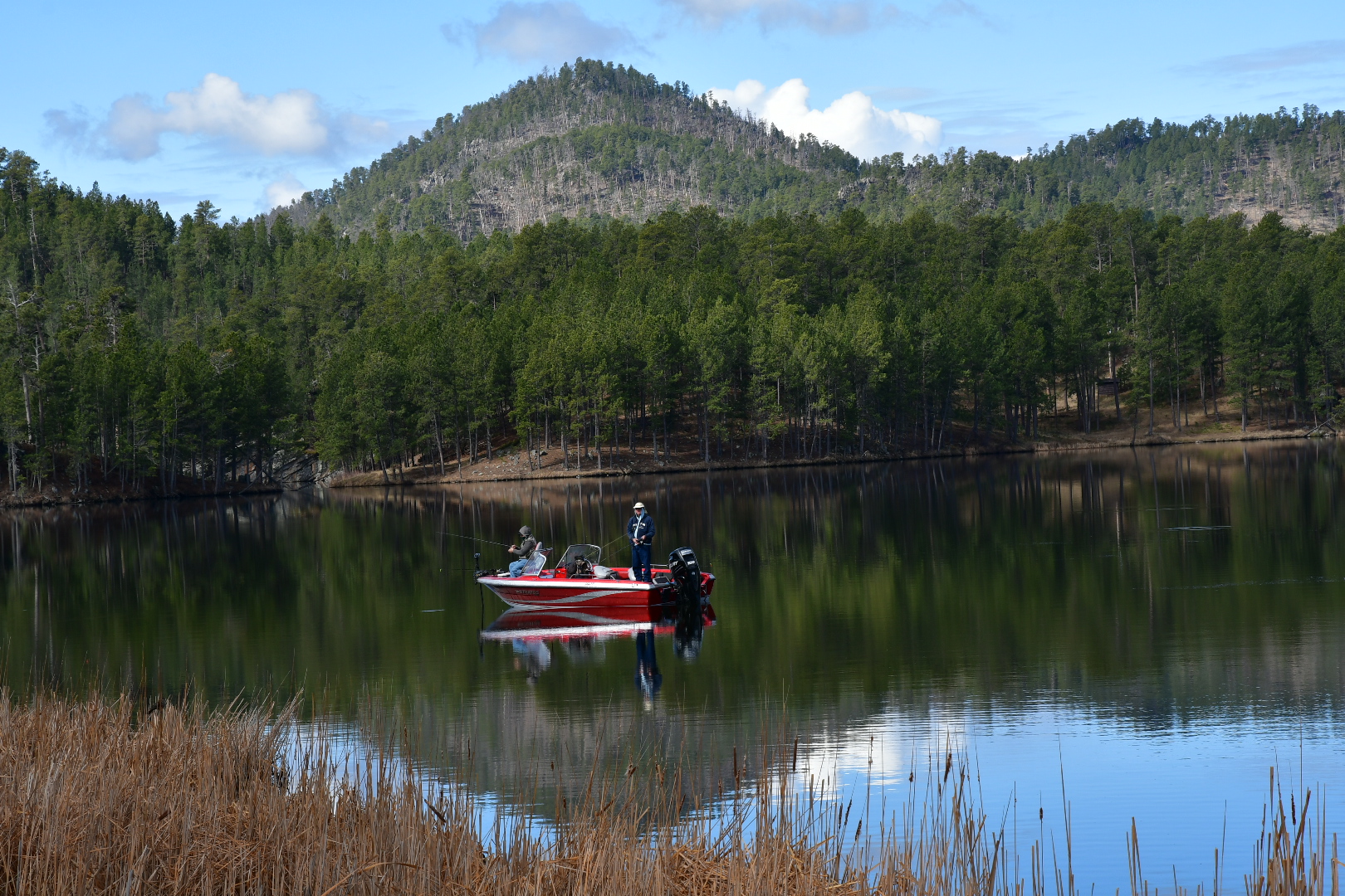 Zwei Angler auf einem rotem Motorboot auf einem See vor bewaldetem Berg in den Black Hills in South Dakota